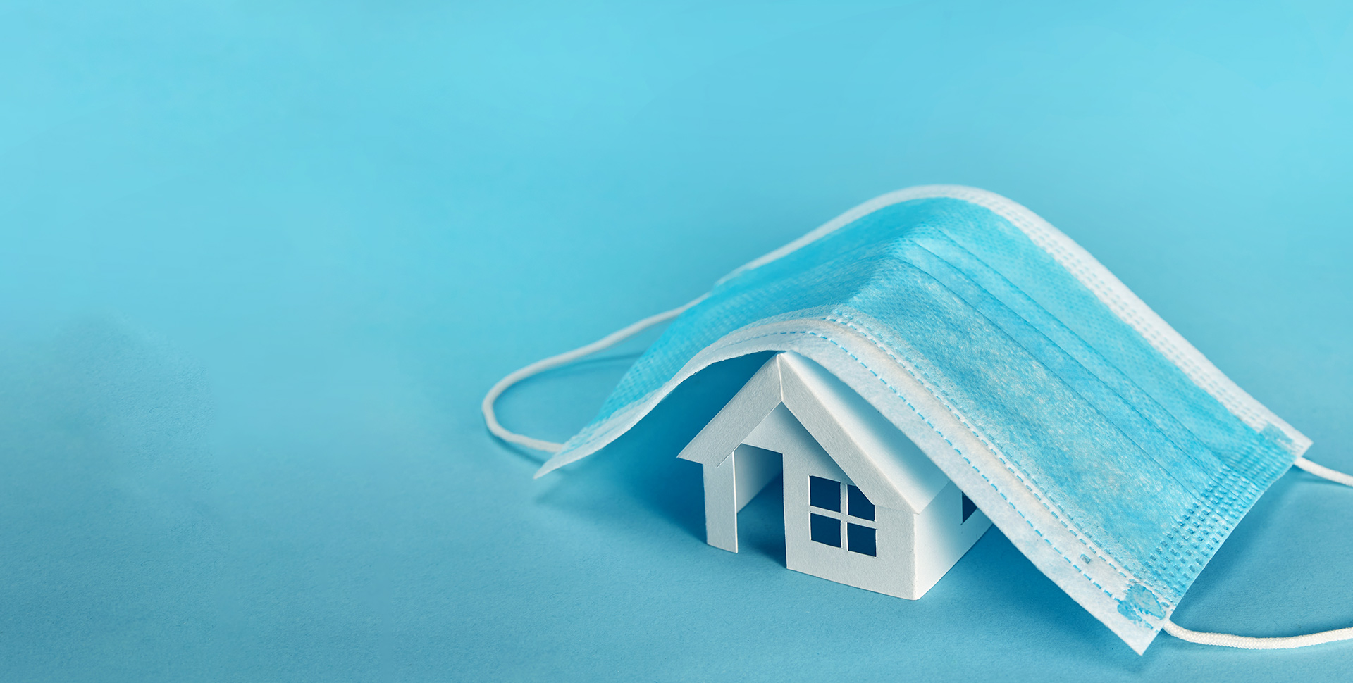 A conceptual image of a medical mask over a paper house.