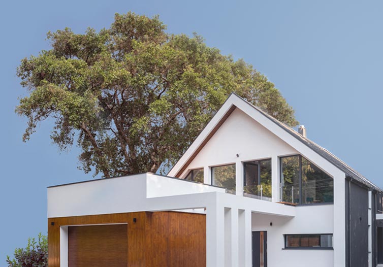 A modern white home surrounded by greenery over a blue sky.