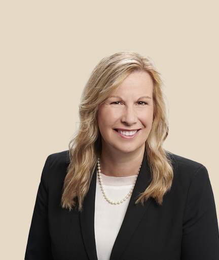 A woman with blonde wavy hair smiles, wearing business attire.