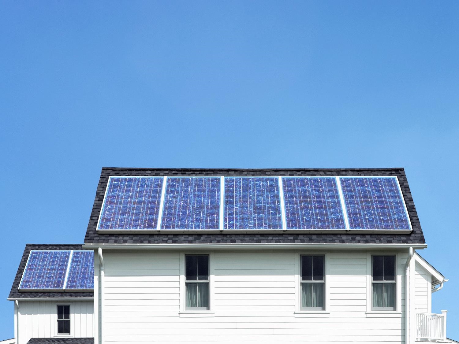 A home with multiple solar panels on the roof over a blue sky.