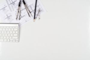 Overhead shot of a desk displaying a keyboard, some drawing tools and an architectural drawing.