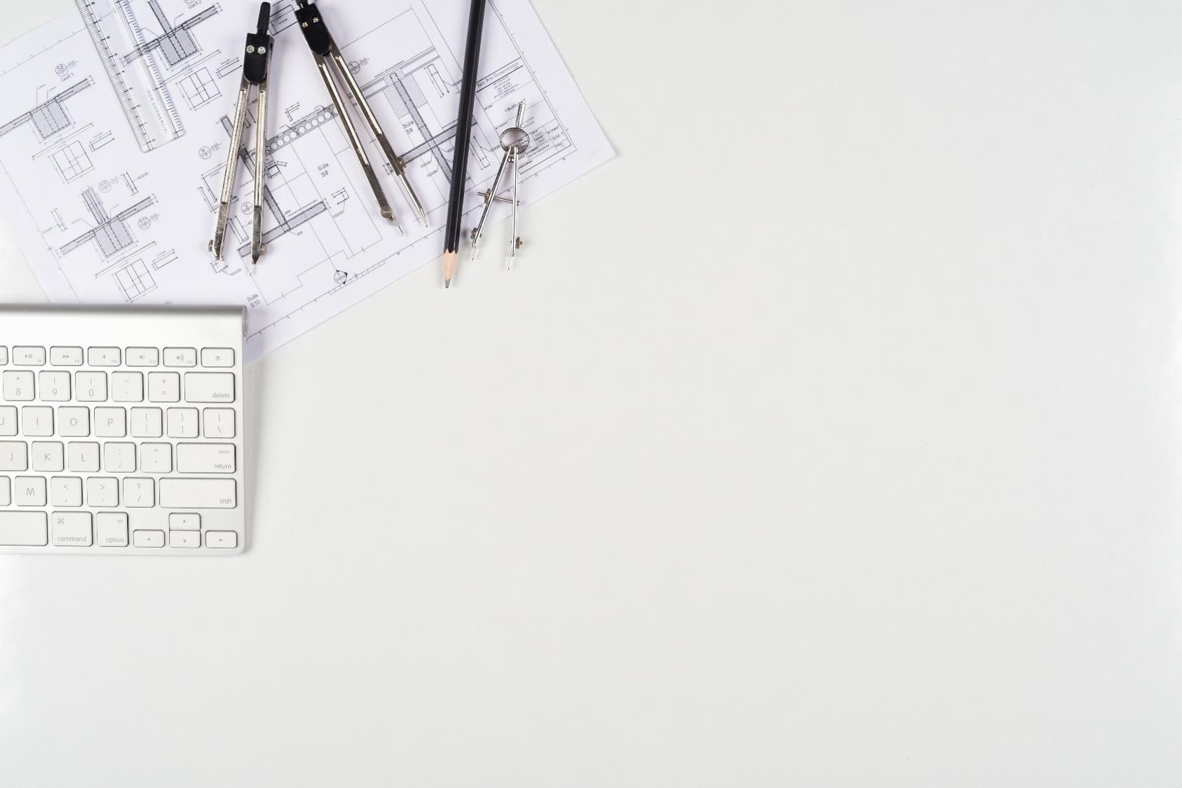 Overhead shot of a desk displaying a keyboard, some drawing tools and an architectural drawing.