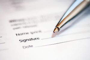 A super close up of a document with a pen over it. The angle suggests an invite to sign the document.