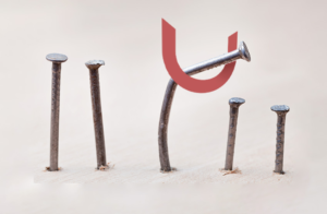 Five nails in a wooden surface, with a red U shape above them. One nail is leaning towards the magnet, while the others stand upright.