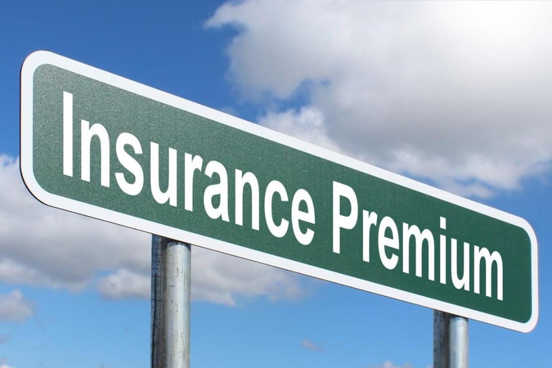 A green road sign with the words Insurance Premium in white text stands against a partly cloudy sky.